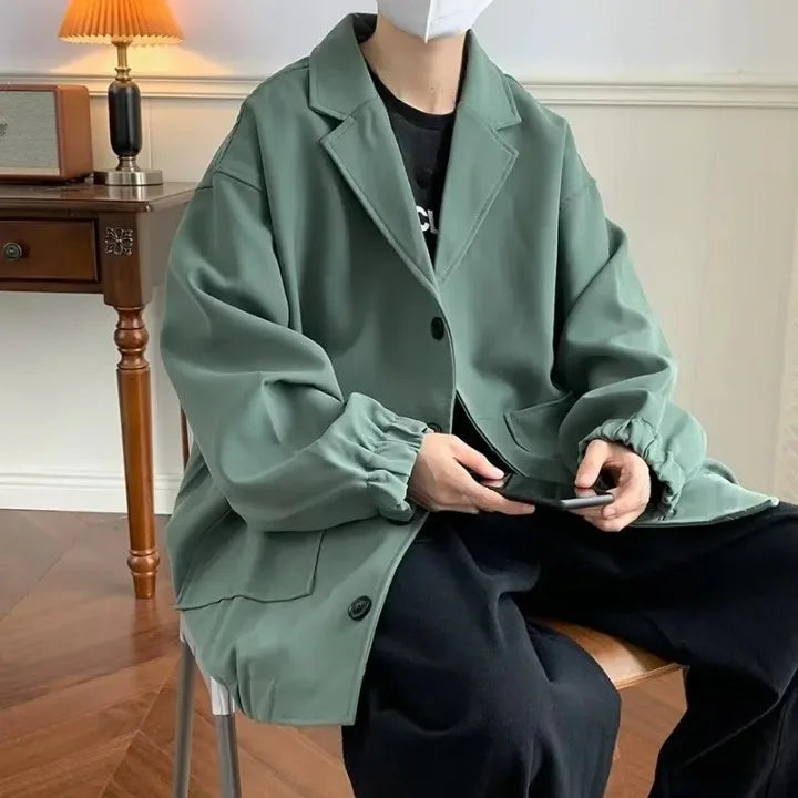 Mann trägt grünen Oversize-Blazer mit lockerem Schnitt, kombiniert mit schwarzem T-Shirt und schwarzen Hosen, moderner Oversize-Look für Herren.