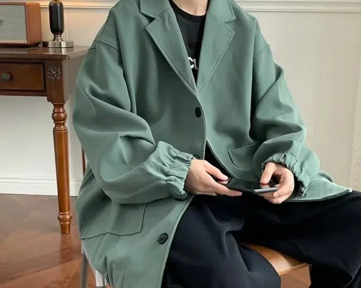 Mann trägt grünen Oversize-Blazer mit lockerem Schnitt, kombiniert mit schwarzem T-Shirt und schwarzen Hosen, moderner Oversize-Look für Herren.